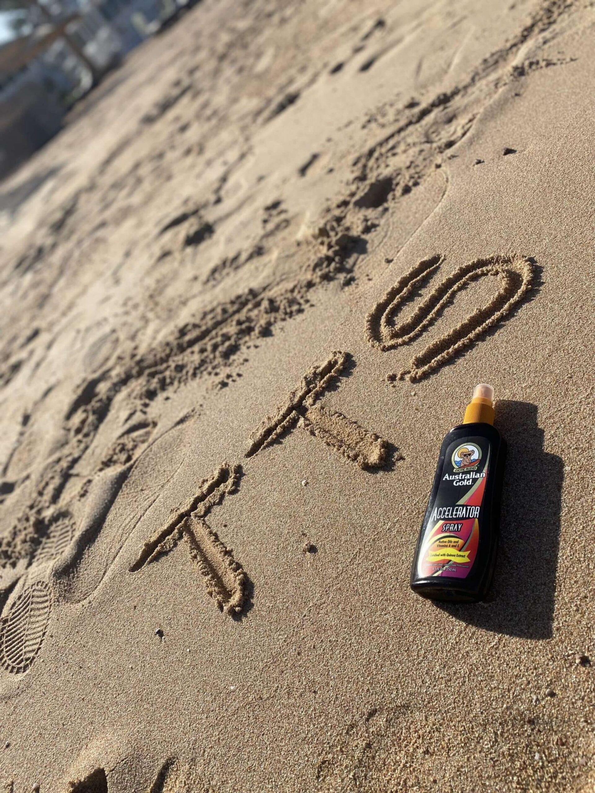 Australian Gold Accelerator tanning lotion on beach with TTS written in sand at The Tanning Shop UK