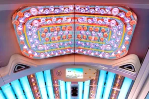 Interior view of Luxura Jewel tanning bed canopy with colourful LED lights, orange accent rings and a control panel showing session time