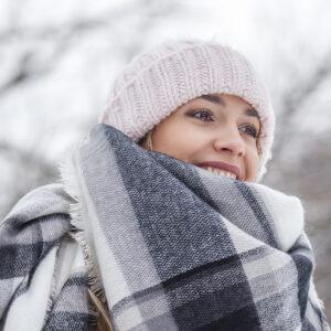 Happy woman in winter hat and scarf smiling outdoors for winter tanning blog