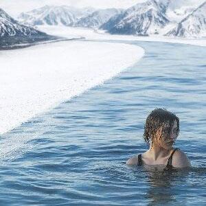 Woman cold water swimming in icy glacial mountain waters - cold water immersion therapy for health and wellbeing