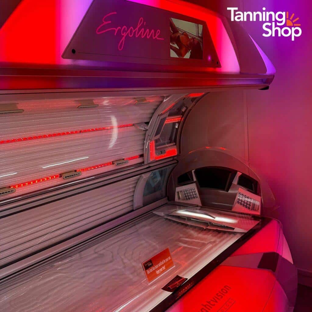 Open Ergoline tanning bed with red LED accent lights in a purple-lit Tanning Shop salon, featuring premium sunbed equipment for professional indoor tanning."