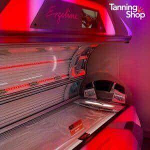 Open Ergoline tanning bed with red LED accent lights in a purple-lit Tanning Shop salon, featuring premium sunbed equipment for professional indoor tanning.