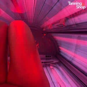 Inside view of a Tanning Shop red light therapy tanning bed session, showing legs bathed in red and pink LED light for skin rejuvenation and tanning benefits.