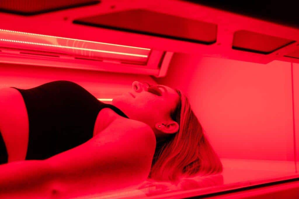 Woman lying in a red light therapy bed bathed in red LED light at The Tanning Shop