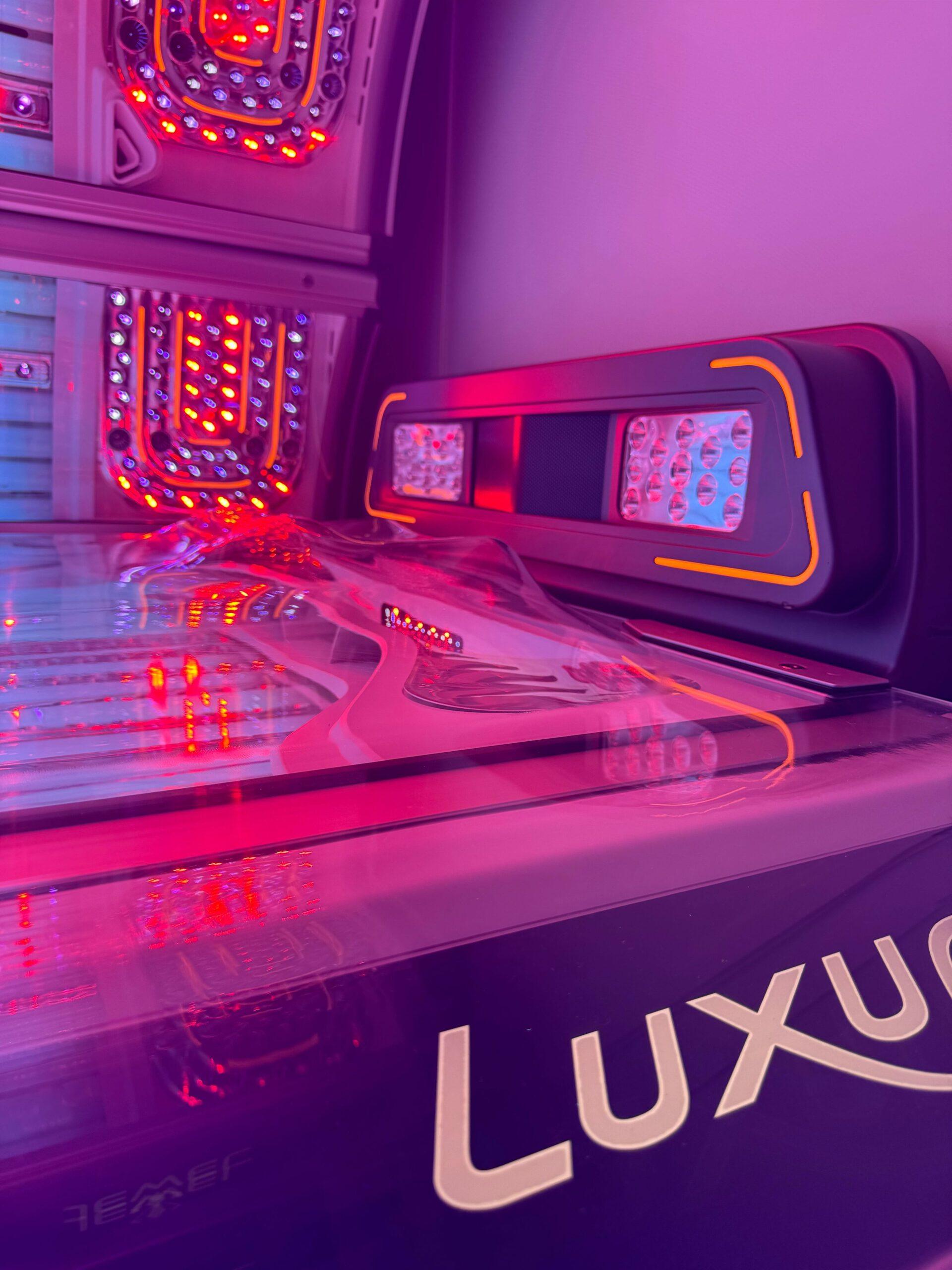 Luxura tanning bed with multi-coloured LED lighting and Luxura branding on the base at The Tanning Shop