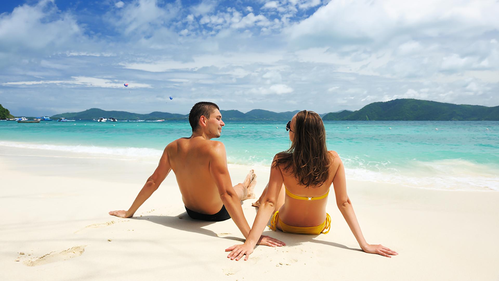 Tanned couple relaxing on tropical beach for sunbed and spray tan packages at The Tanning Shop UK